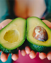 Woman holds sliced avacado as nutrition for health and wellbeing in integrative addiction care and recovery.